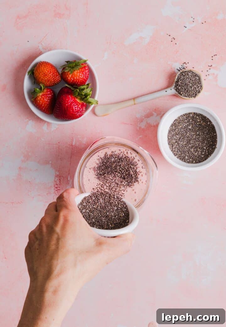 Woman's hand pouring chia seeds into strawberry milk in a glass jar