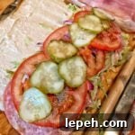 An open faced sandwich with pickles, tomato, and salami showing