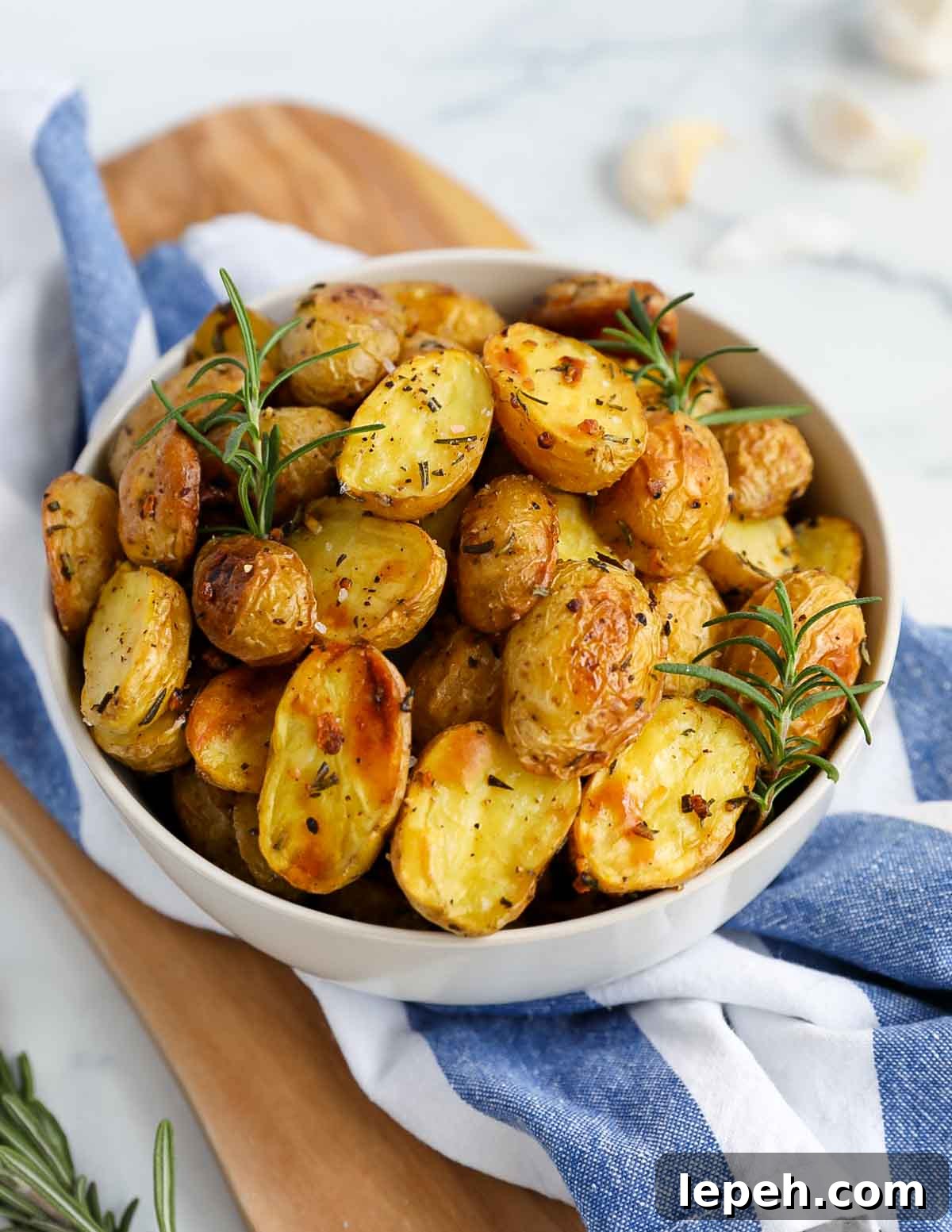 Golden yellow baby potatoes in a large white bowl with fresh rosemary on top.