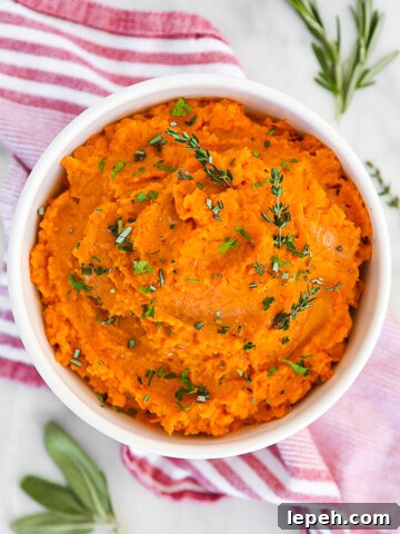 Orange mashed potatoes in a white bowl, garnished with fresh green herbs.