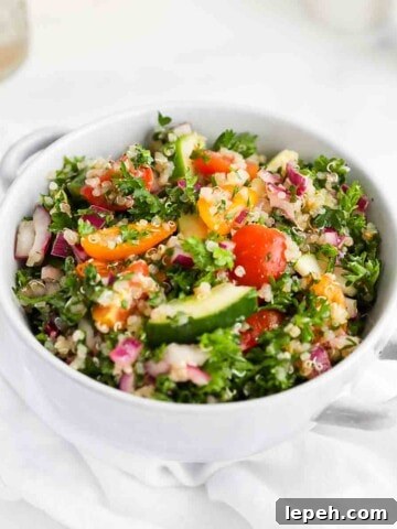 A light blue bowl filled with parsley, quinoa, tomatoes, onion, and cucumbers