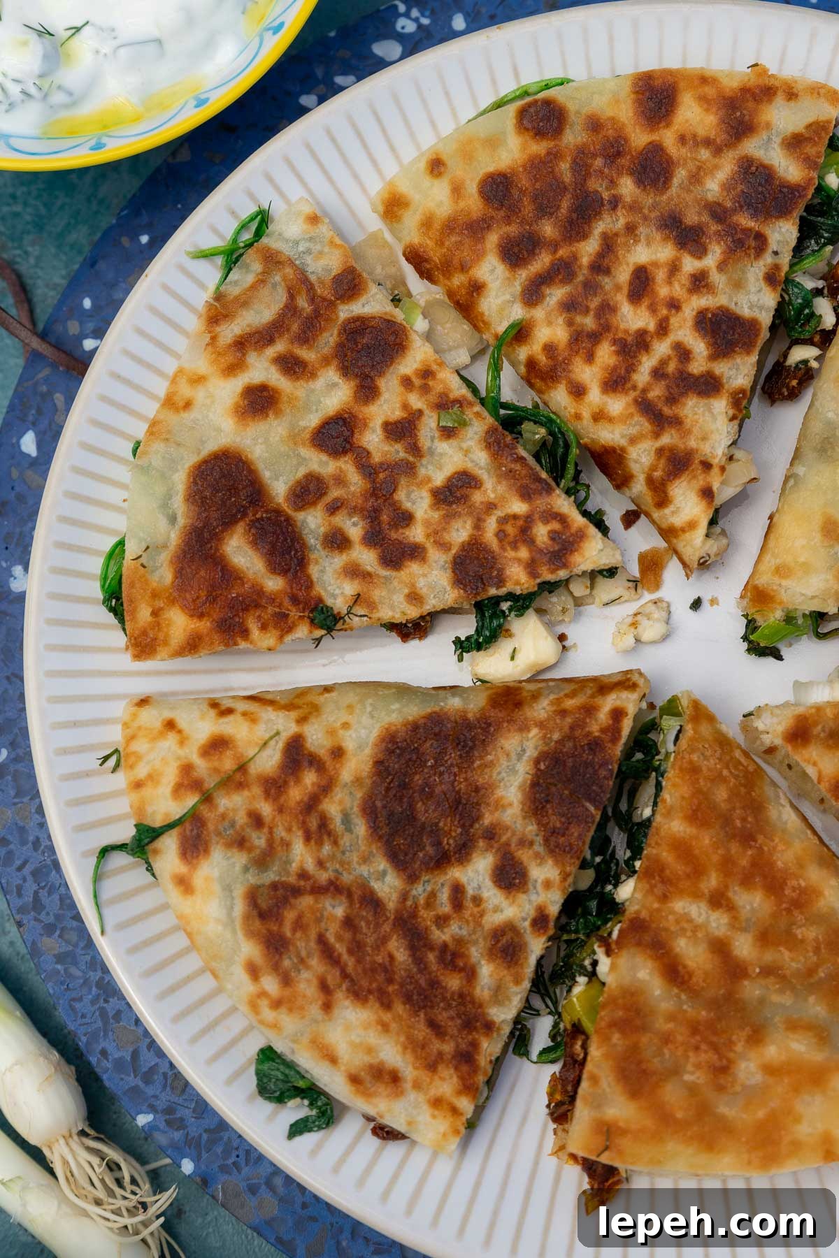 Overhead view of Greek quesadilla triangles arranged in a circle on a white plate.