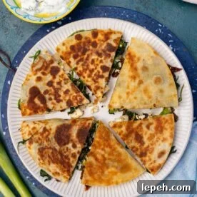 Greek quesadilla triangles arranged in a circle on a white plate with blue tea towel and ingredients around it.