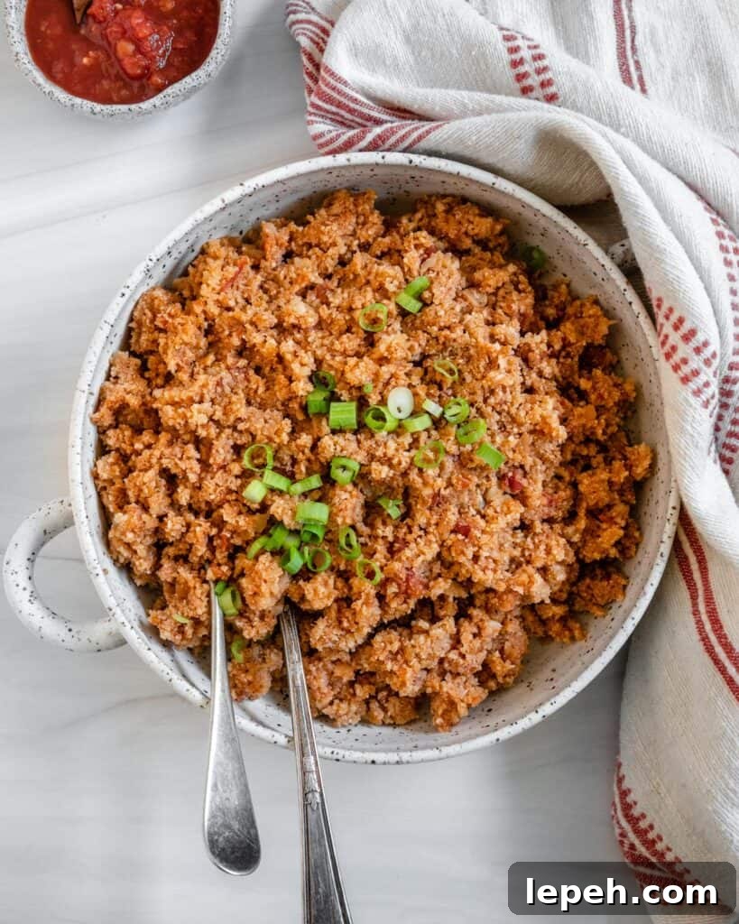 completed Spanish Cauliflower Rice in a white bowl against a white surface with two utensils in the bowl