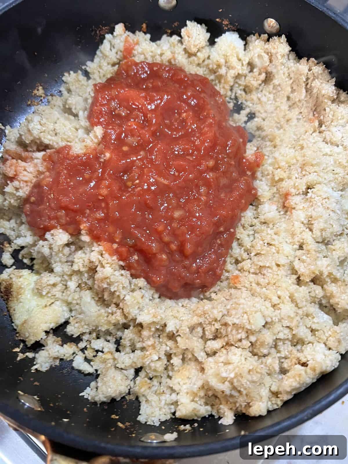 addition of salsa to cauliflower rice in black pan