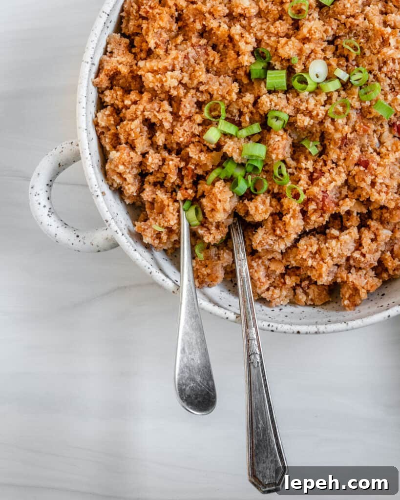 completed Spanish Cauliflower Rice in a white bowl against a white surface with two utensils in the bowl