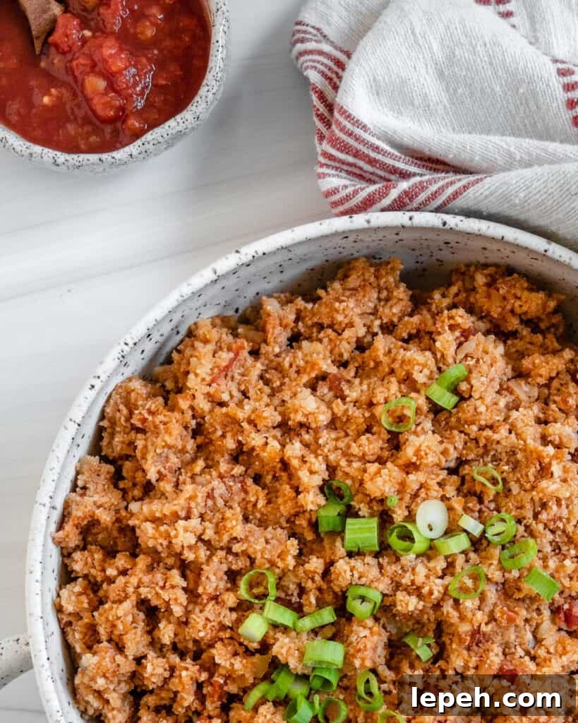 completed Spanish Cauliflower Rice in a white bowl against a white surface with salsa in the background