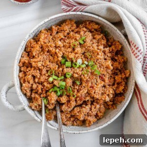 completed Spanish Cauliflower Rice in a white bowl against a white surface with two utensils in the bowl