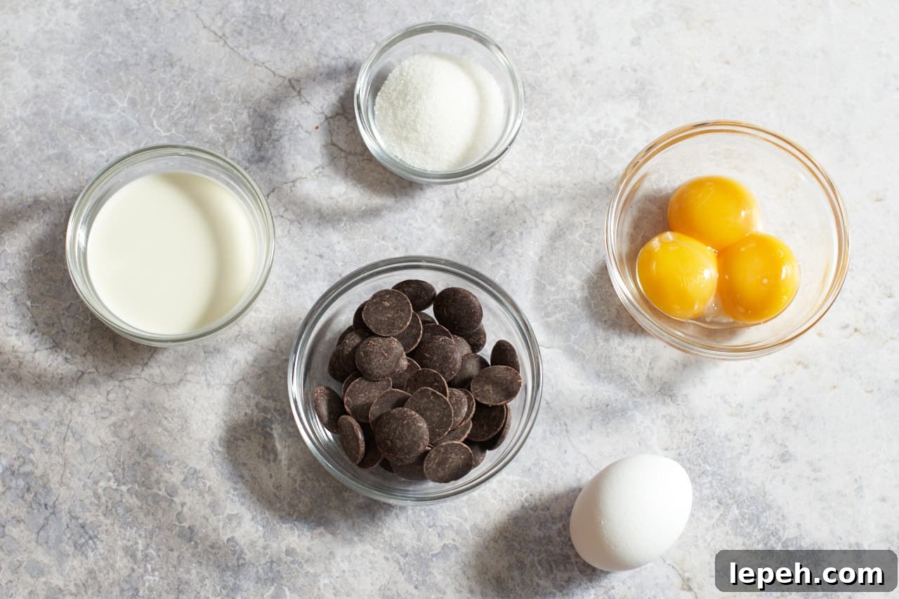 One egg and small glass bowls of egg yolks, sugar, chocolate and heavy cream.