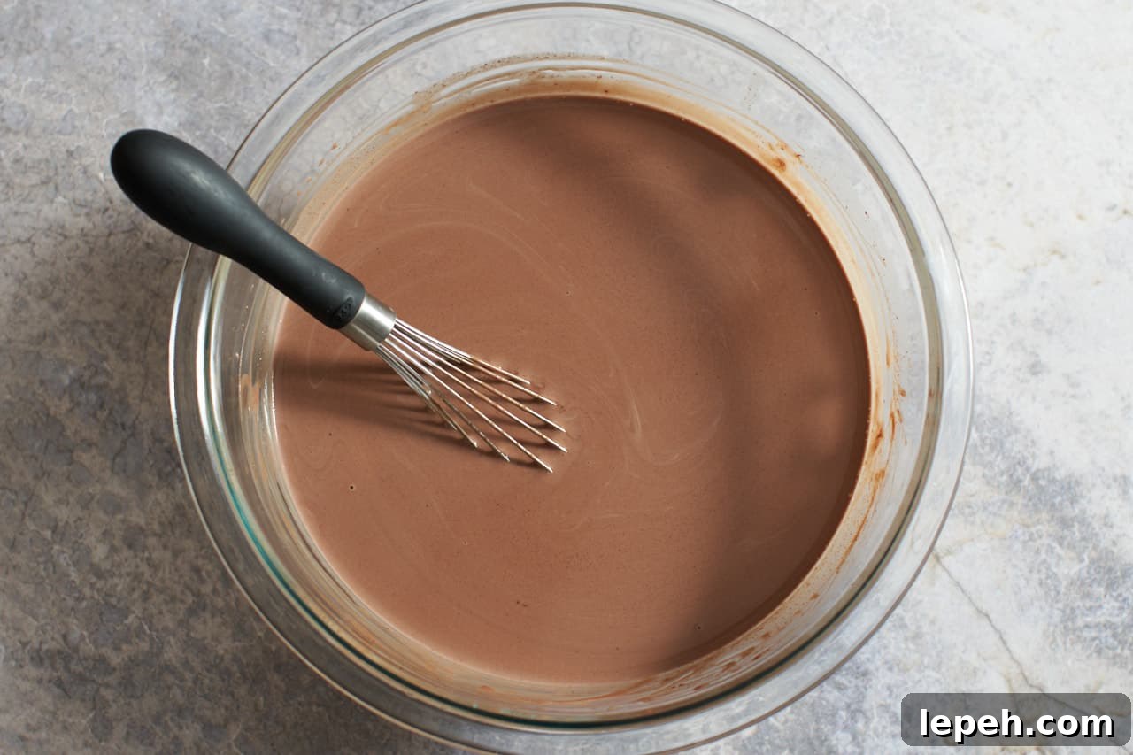 A bowl of melted chocolate and heavy cream with a whisk in it.