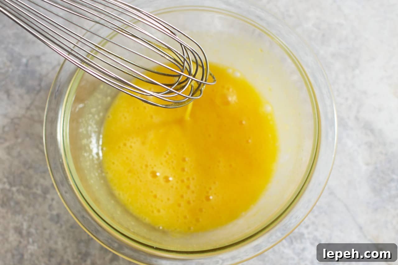 A whisk in a bowl of eggs mixed with sugar.