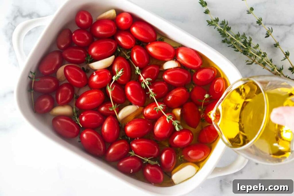 Pouring olive oil in a dish with tomatoes, garlic and thyme sprigs.