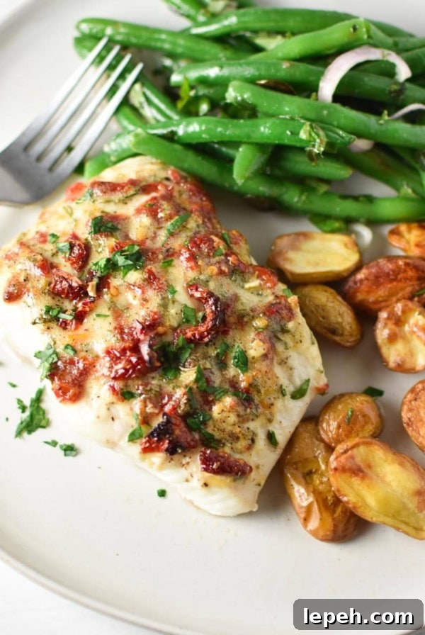 A filet of mediterranean baked halibut on a white plate with potatoes and green beans.
