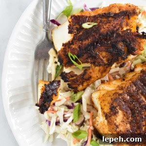A fork holding a piece of blackened code next to two filets on top of coleslaw
