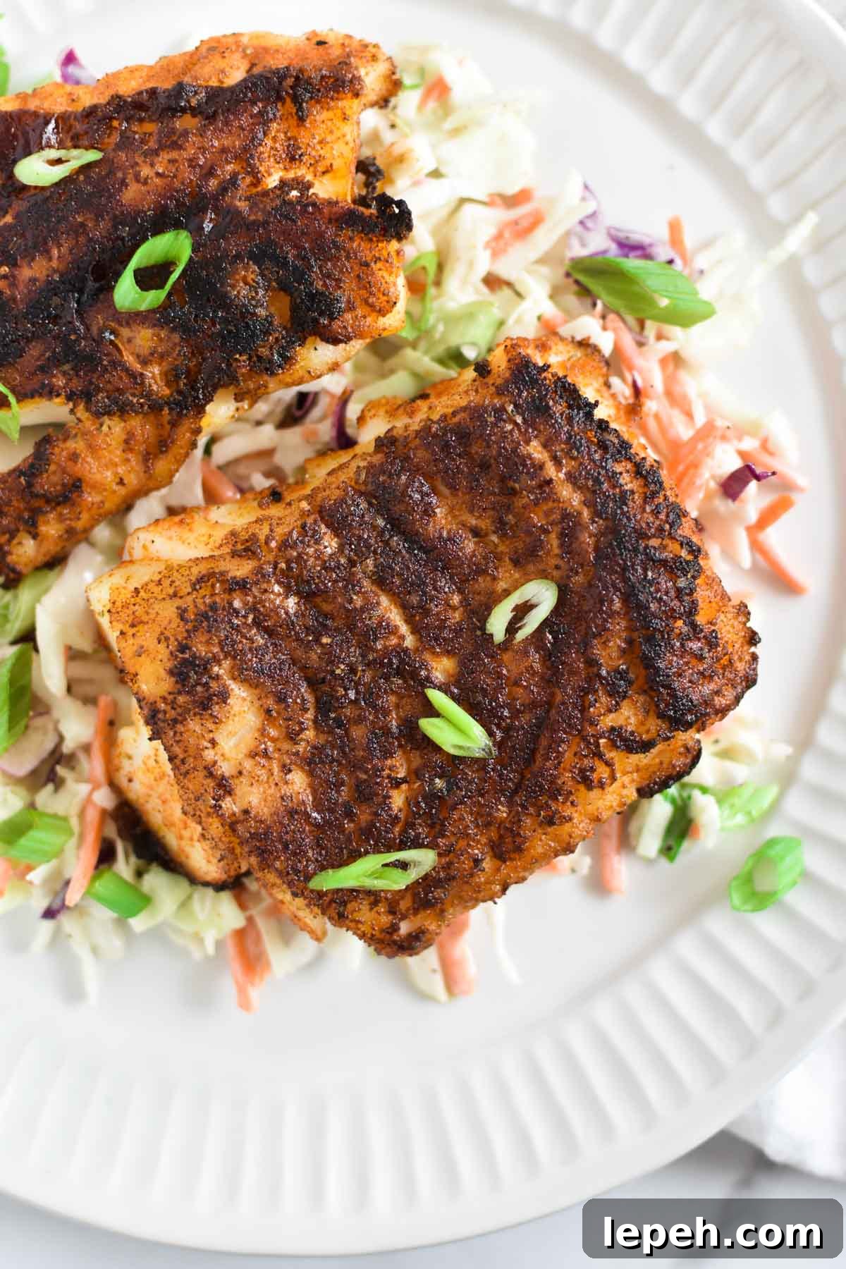 Blackened fish on a white plate with green onions on top