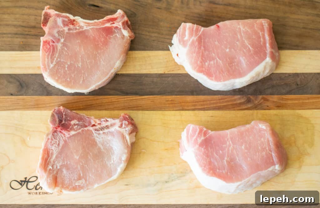 2 bone in pork chops and 2 boneless pork chops on a wooden cutting board.