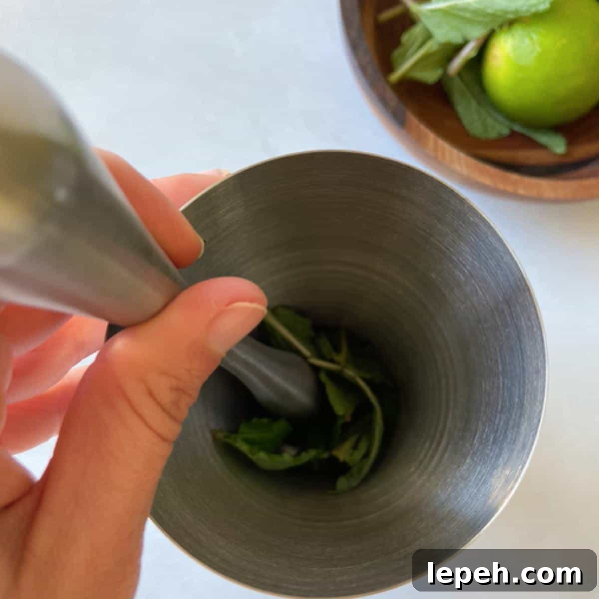 Hand muddling mint in stainless steel shaker.