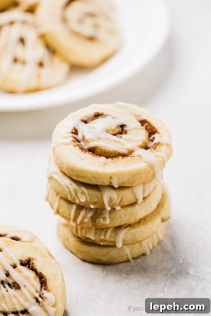 stack of cinnamon roll cookies with icing. Plate of cookies behind stack