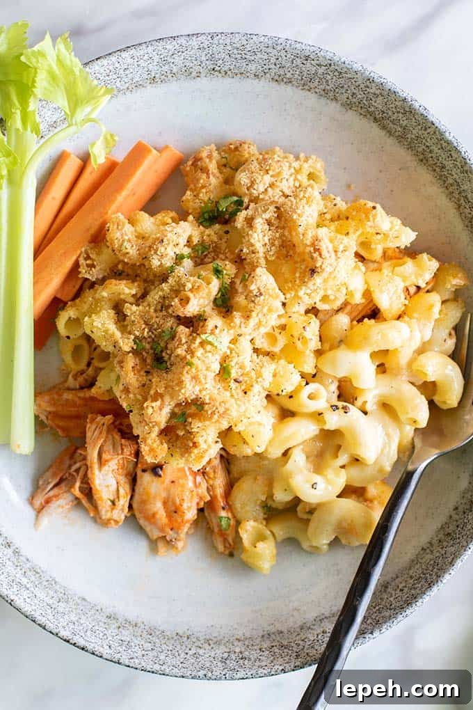 A close up view of a baked buffalo chicken mac and cheese served with carrots and celery.