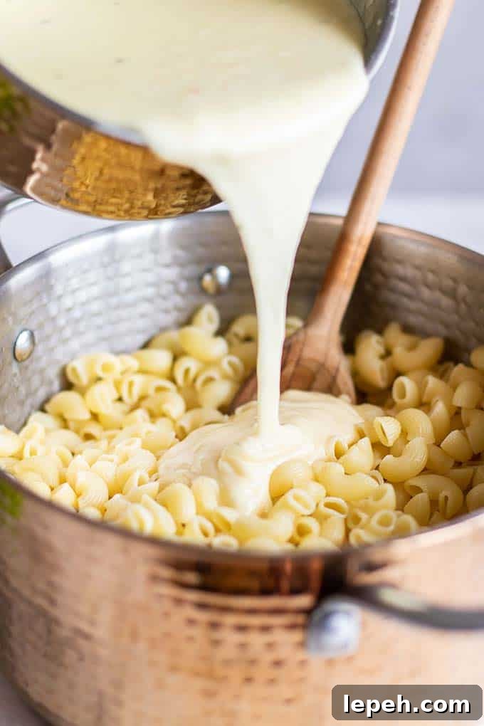 A white cheddar cheese sauce being poured onto a pan of macaroni noodles.