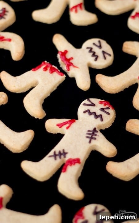 Flat lay view of lots of decorated ginger-dead men Halloween biscuits against a black background.