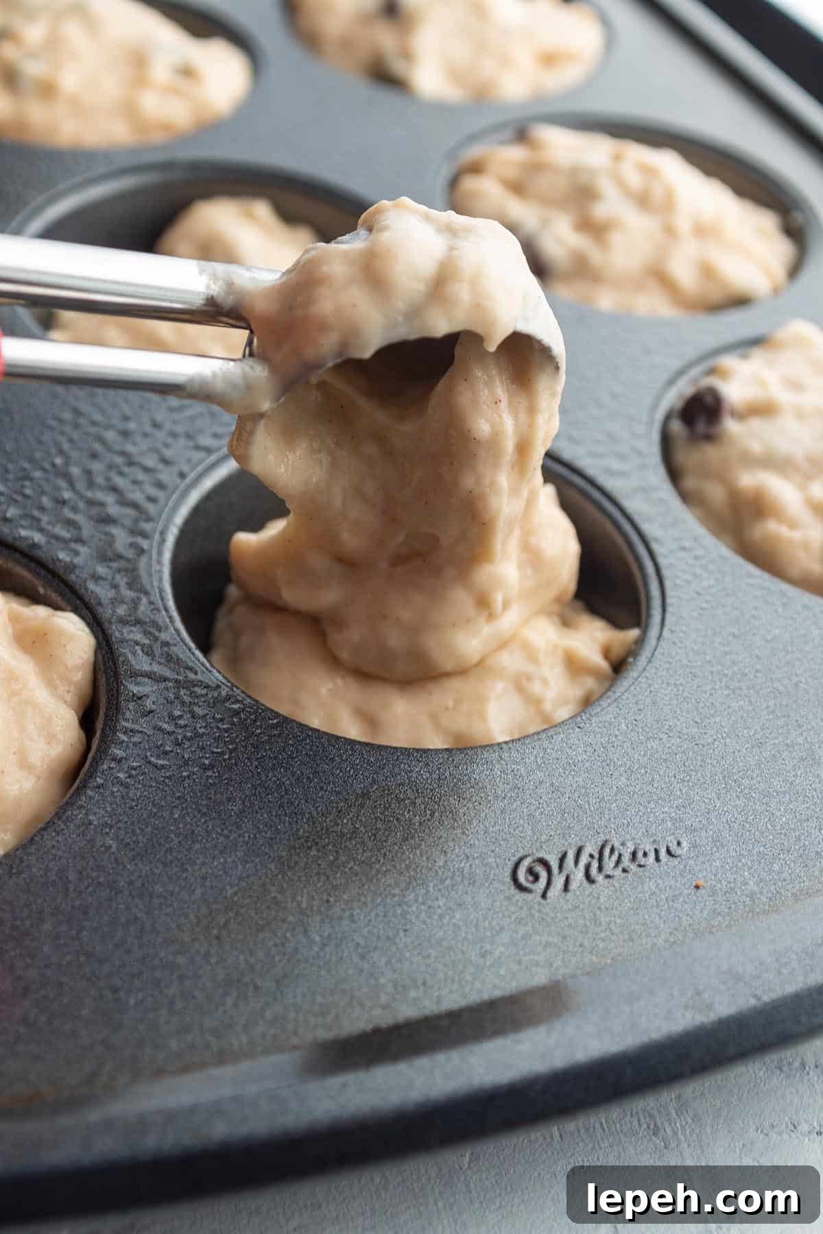 A cookie scoop dividing out muffin batter into a baking pan.