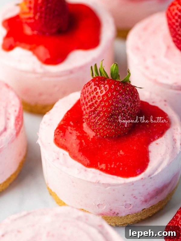 Individual no-bake strawberry cheesecakes topped with strawberry glaze and a fresh strawberry on a parchment paper-lined baking sheet.