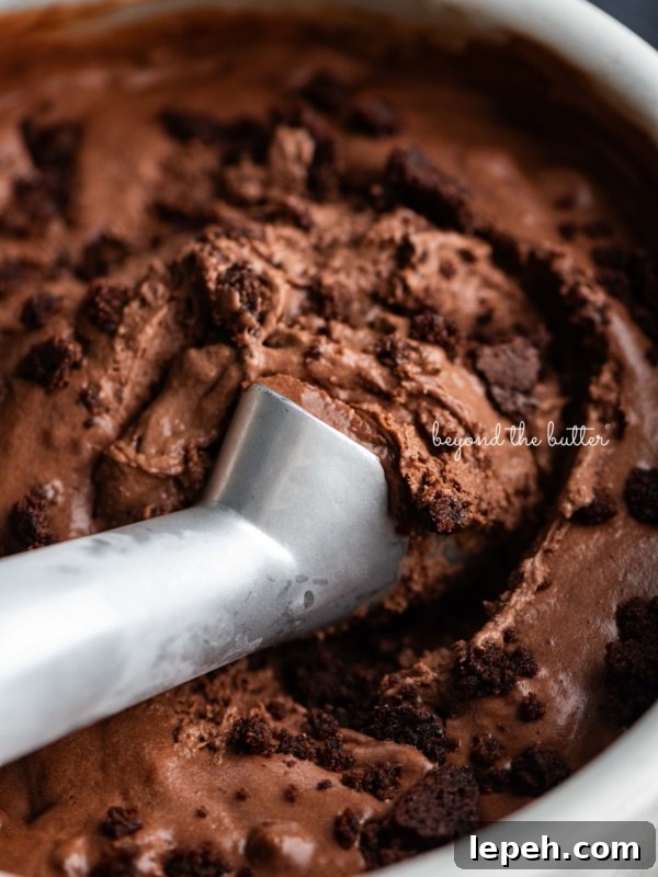 Scooping chocolate brownie ice cream out of a round stainless steel container with a chilled ice cream scoop.