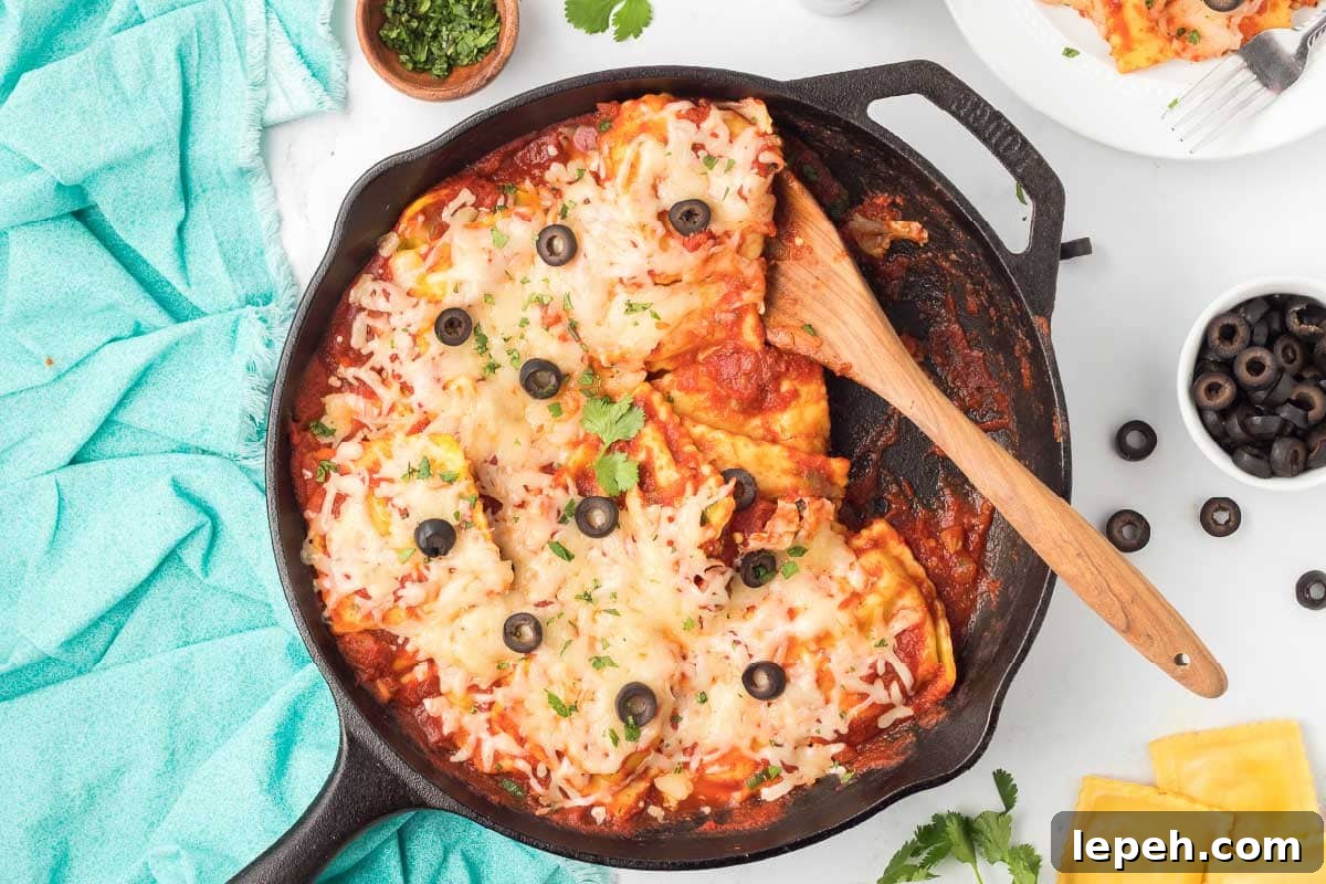 Cast iron skillet with cooked ravioli mixed with salsa, herbs, and tomato sauce and topped with cheese, black olives, and cilantro.