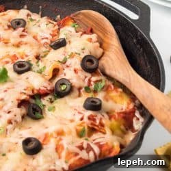 Cast iron skillet with cooked ravioli mixed with salsa, herbs, and tomato sauce and topped with cheese, black olives, and cilantro.