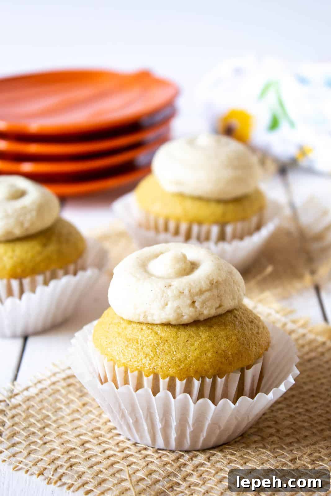 A cupcake with a dollop of frosting on a board with a piece of burlap.