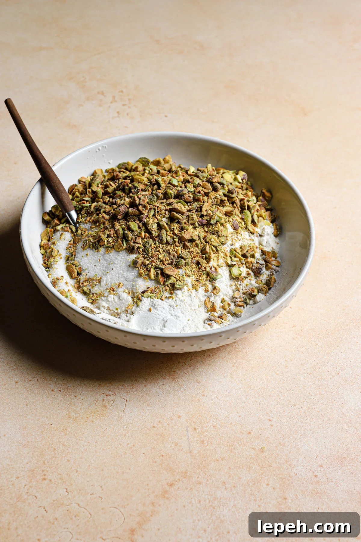 A bowl with flour mixture and chopped pistachio and a fork.