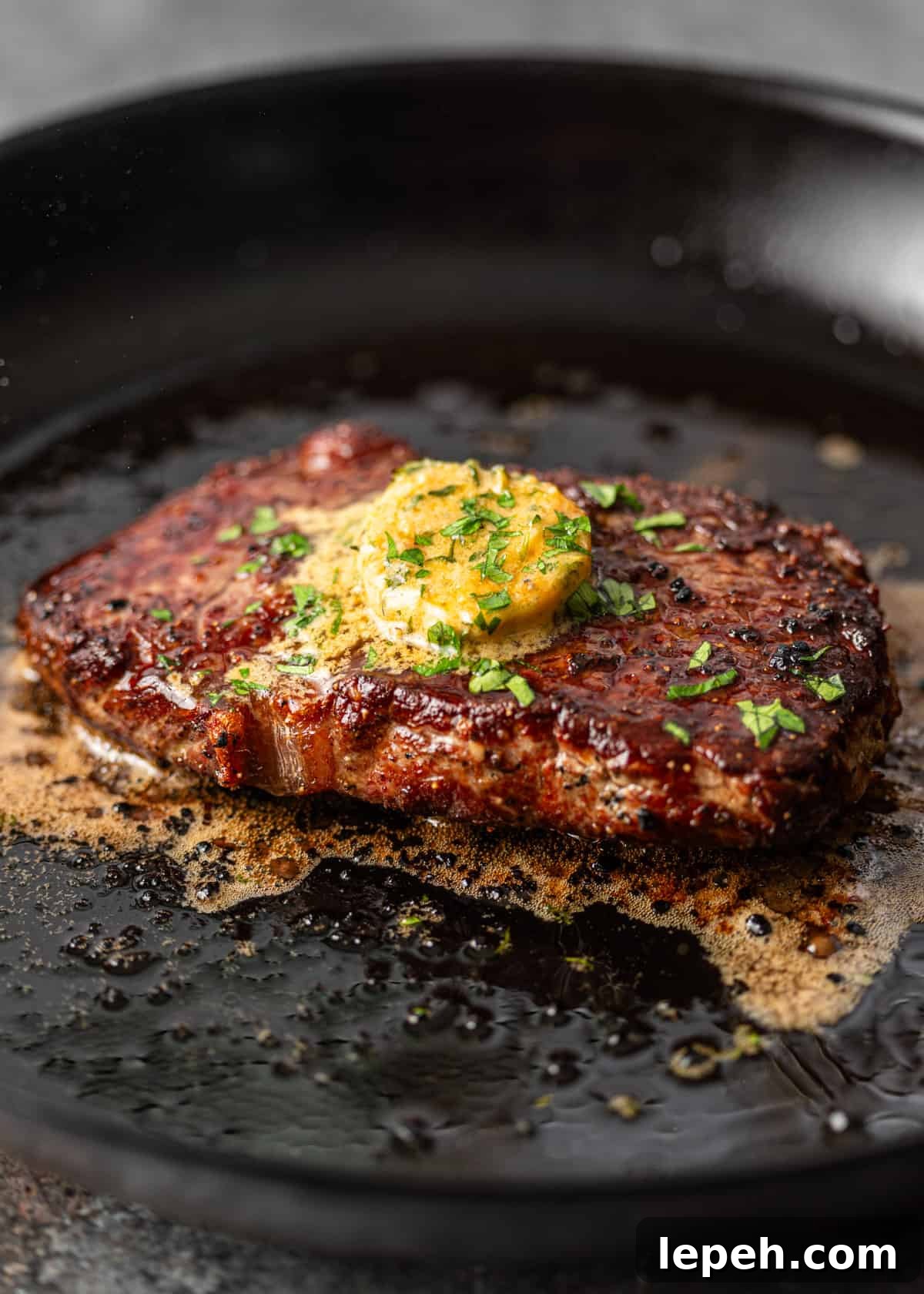 closeup: a steak cooking with a pat of cowboy butter in a skillet