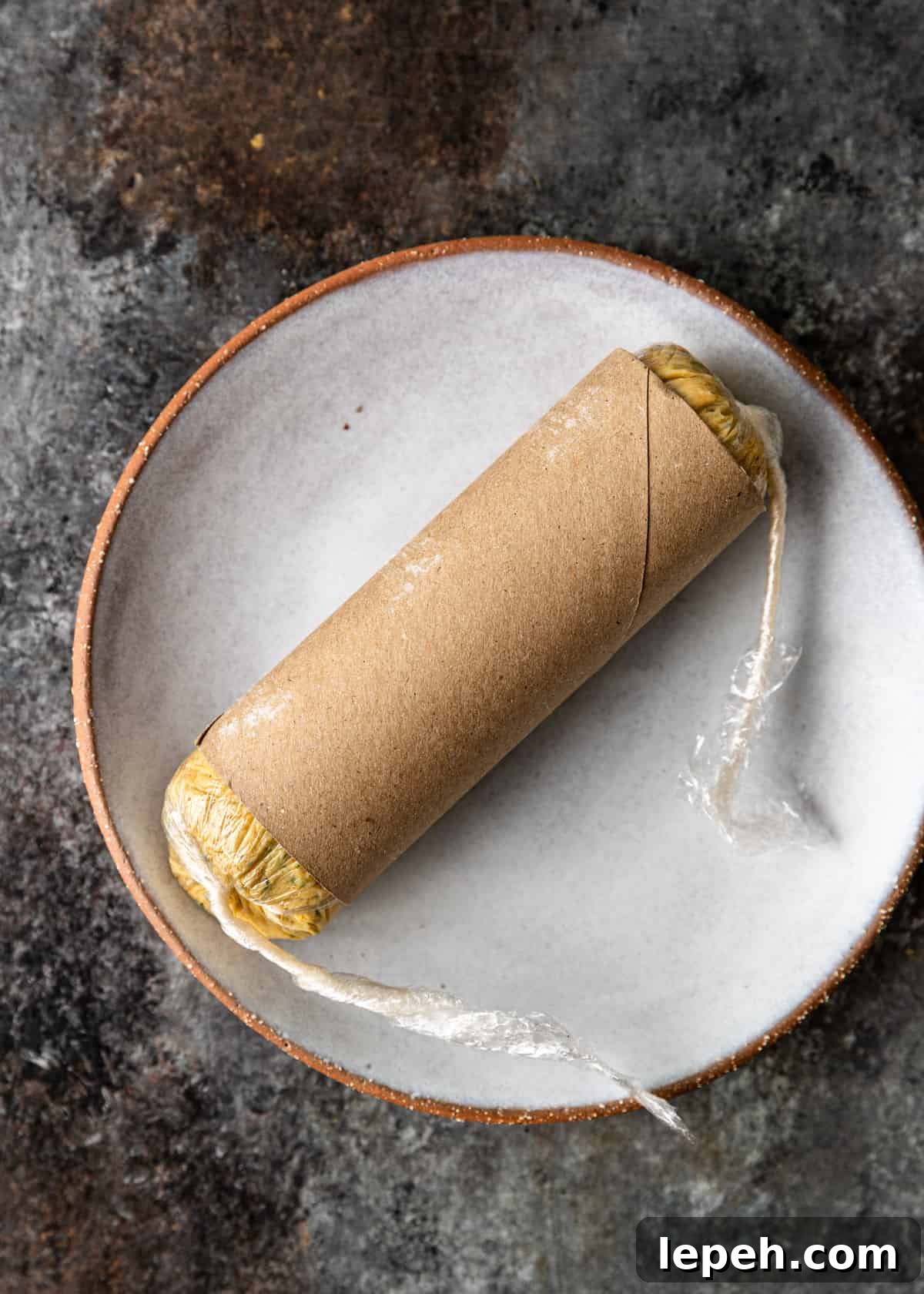 overhead process shot: cowboy butter recipe wrapped in plastic with a paper roll to form