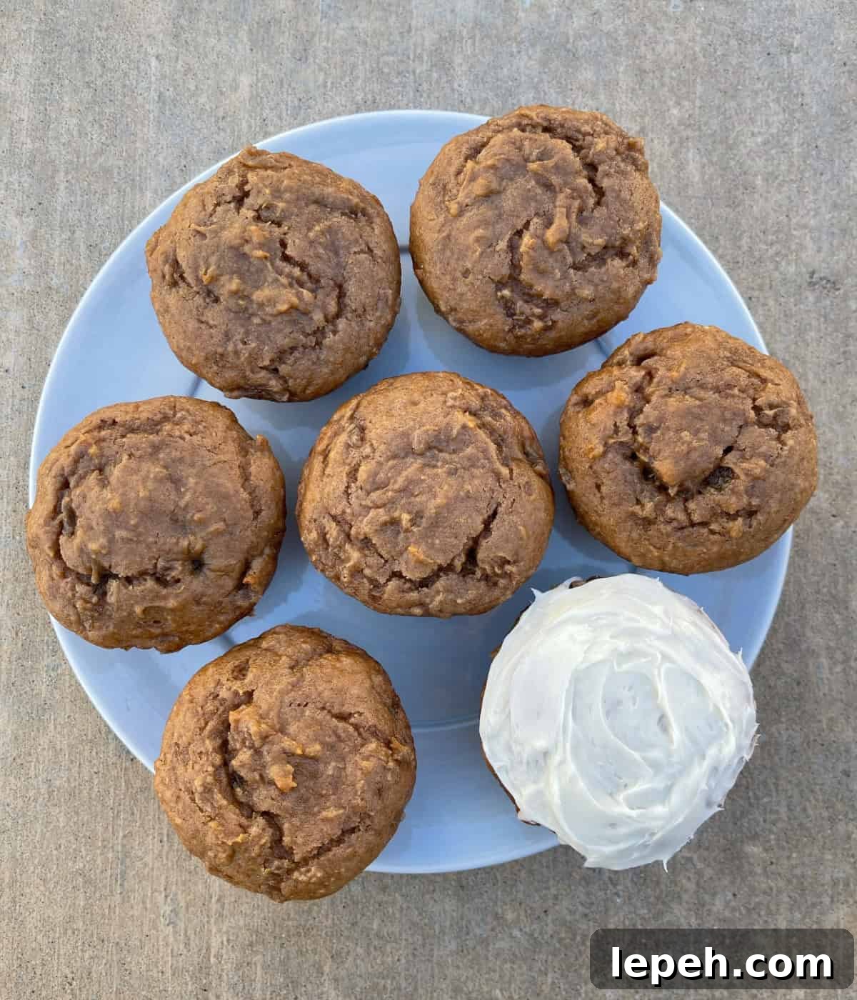 Fresh baked apple spice cake mix cupcakes, one with frosting, on blue serving plate.
