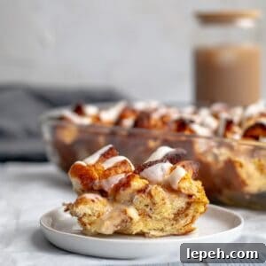 piece of cinnamon roll casserole on a white plate with the baking dish behind