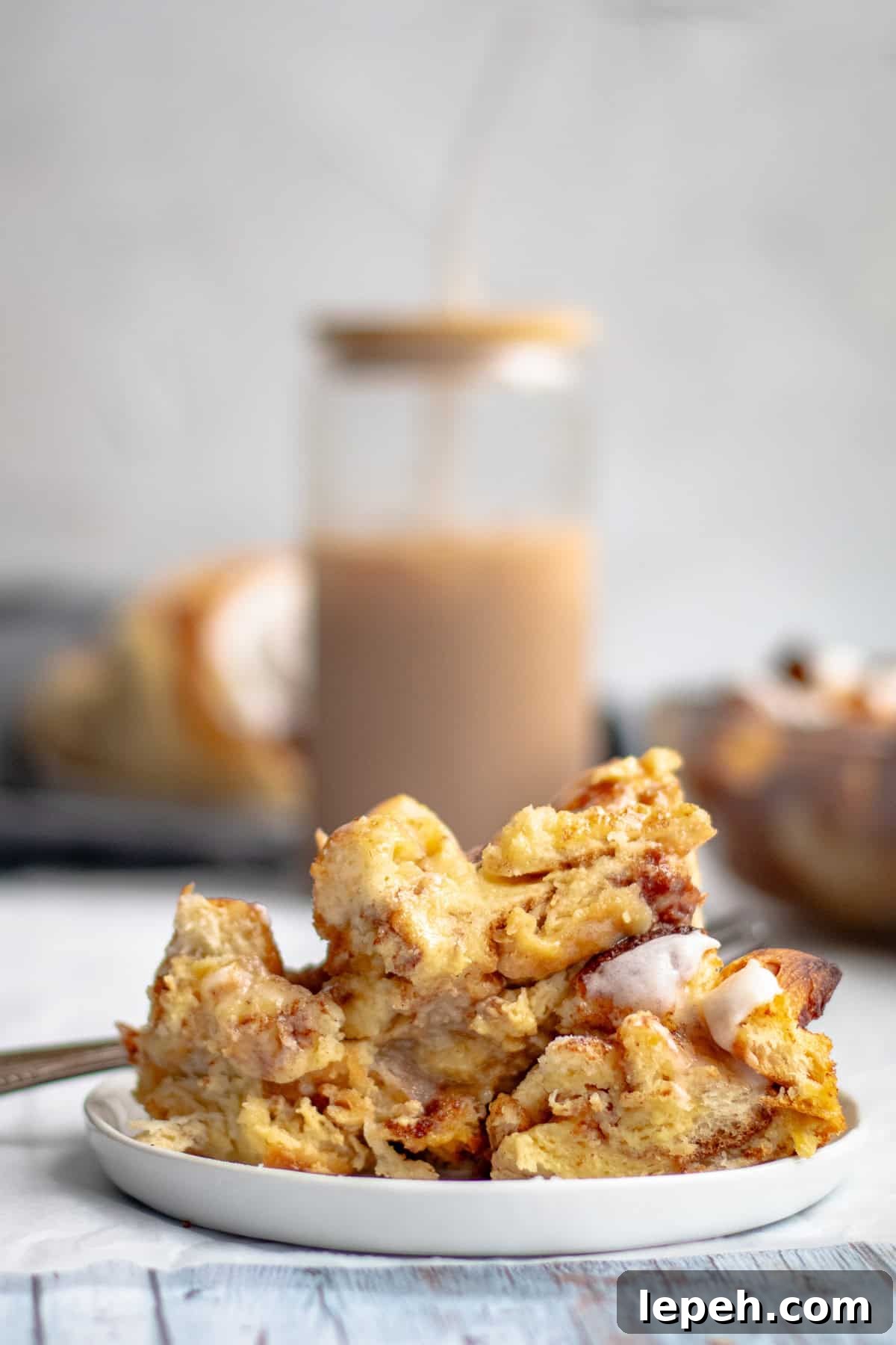 cinnamon roll casserole on a white plate with an iced coffee it the background.