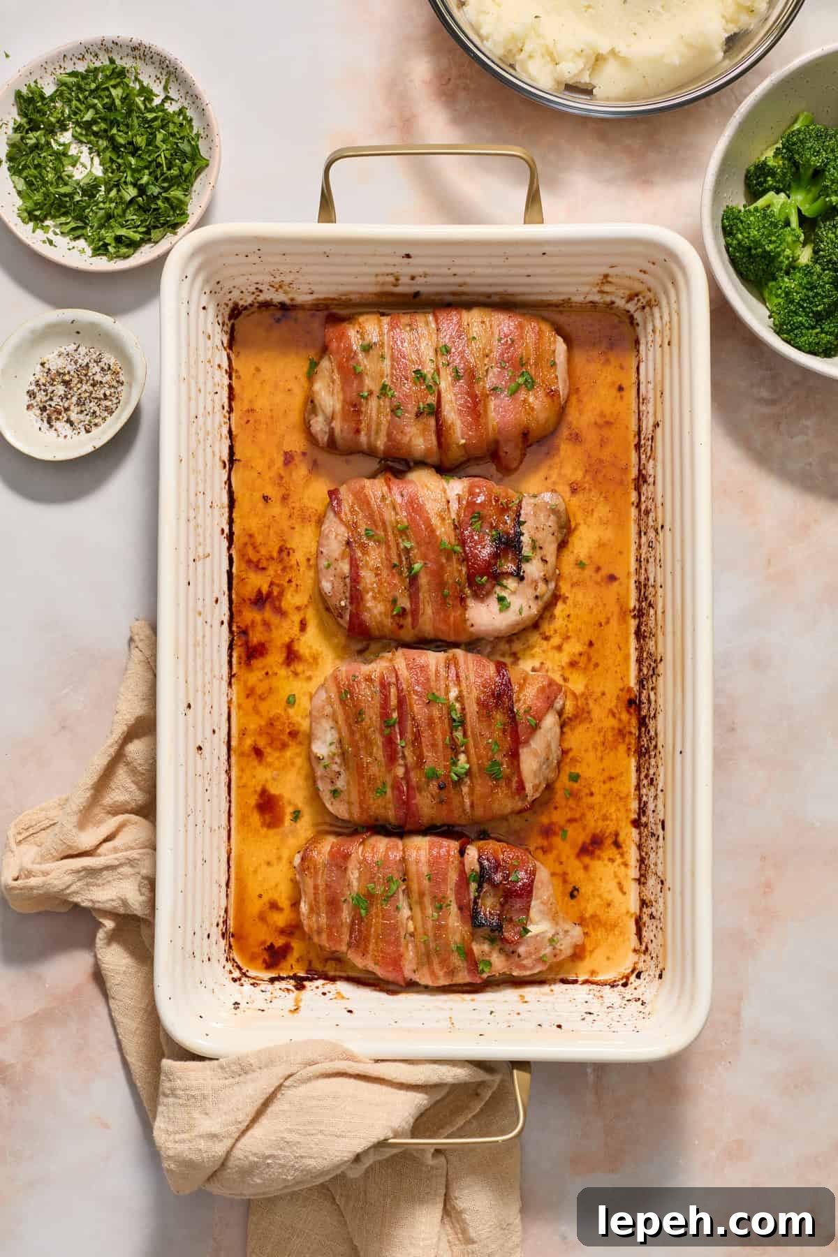 Maple bacon wrapped pork chops in baking pan topped with parsley.