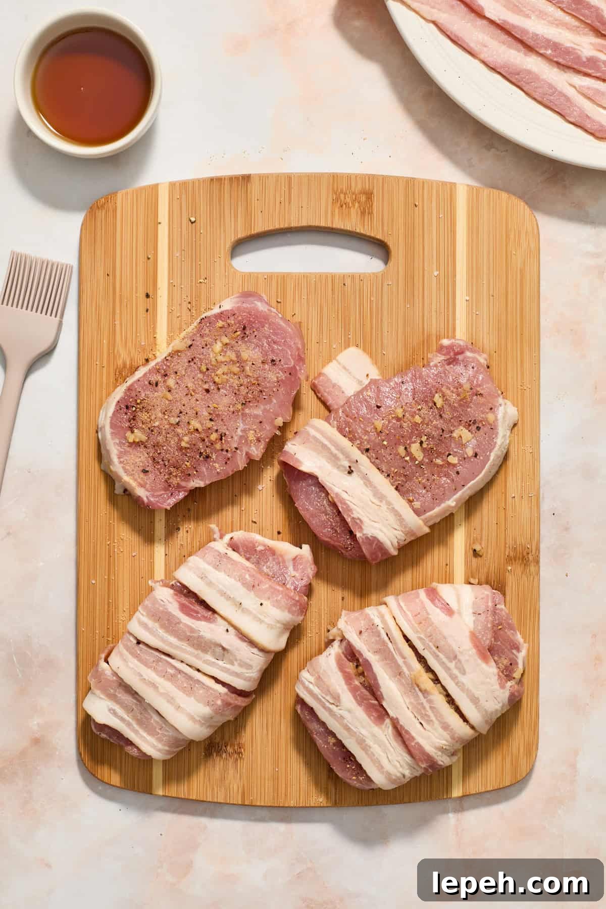 Pork chops with bacon strips wrapped around on cutting board.
