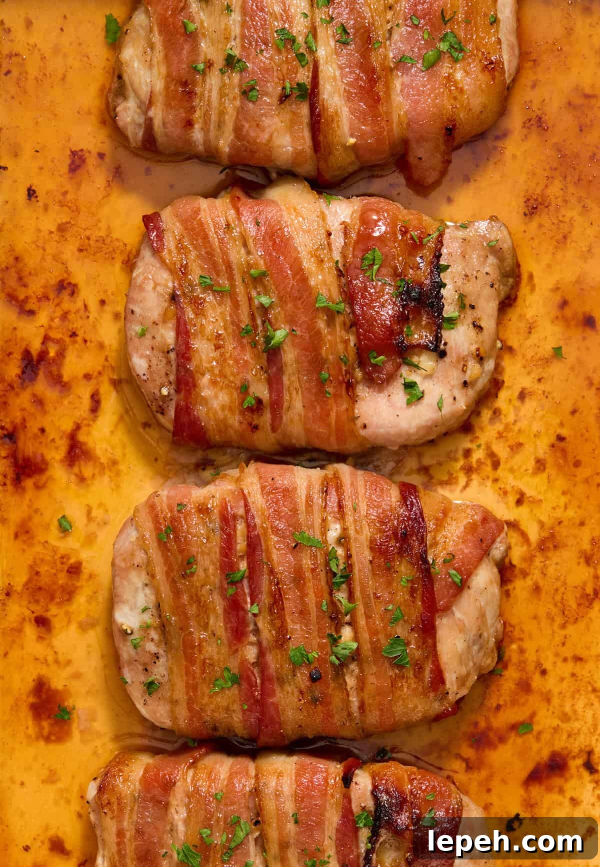 Close up view of bacon wrapped pork chops in pan topped with chopped parsley.