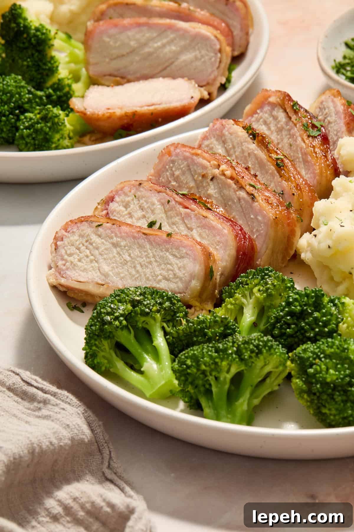 Sliced of pork chop wrapped in bacon on dish with broccoli and potatoes.