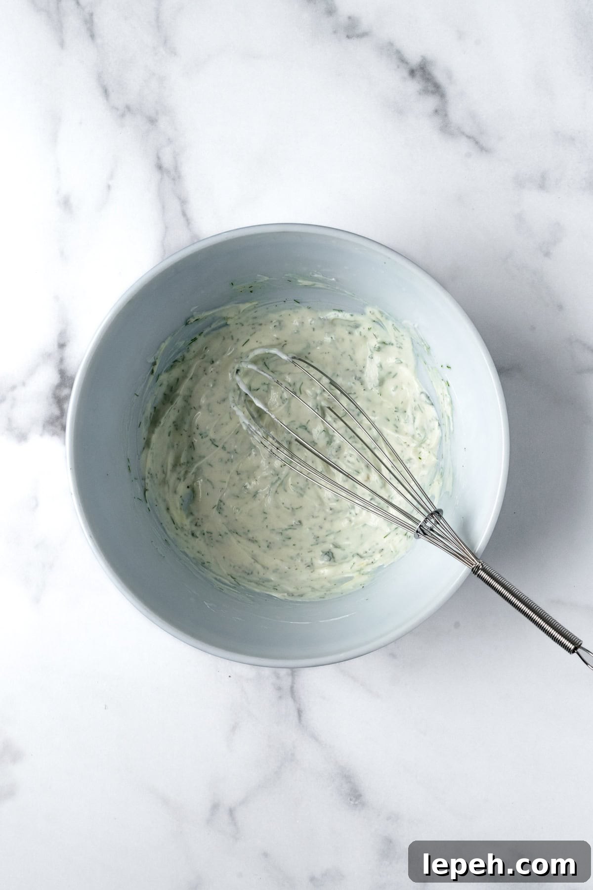 Greek Yogurt Dressing in a white bowl with a whisk.