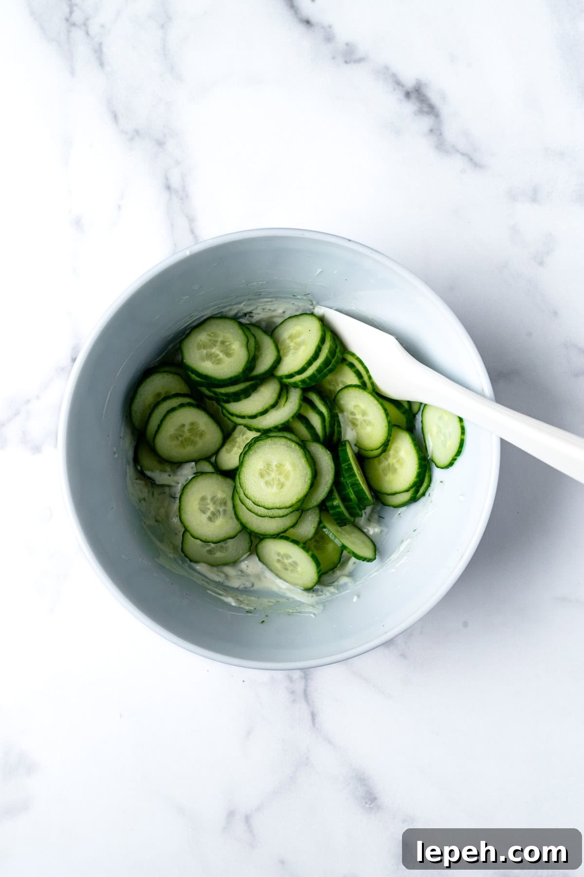 Creamy Dressing and Cucumbers in Bowl with Silicone Spatula.