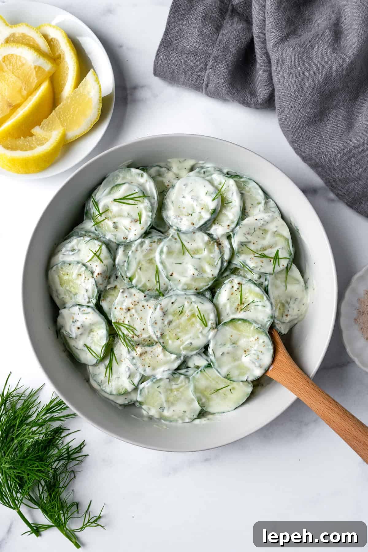 Greek Yogurt Cucumber Salad in a white bowl with a wooden serving spoon.